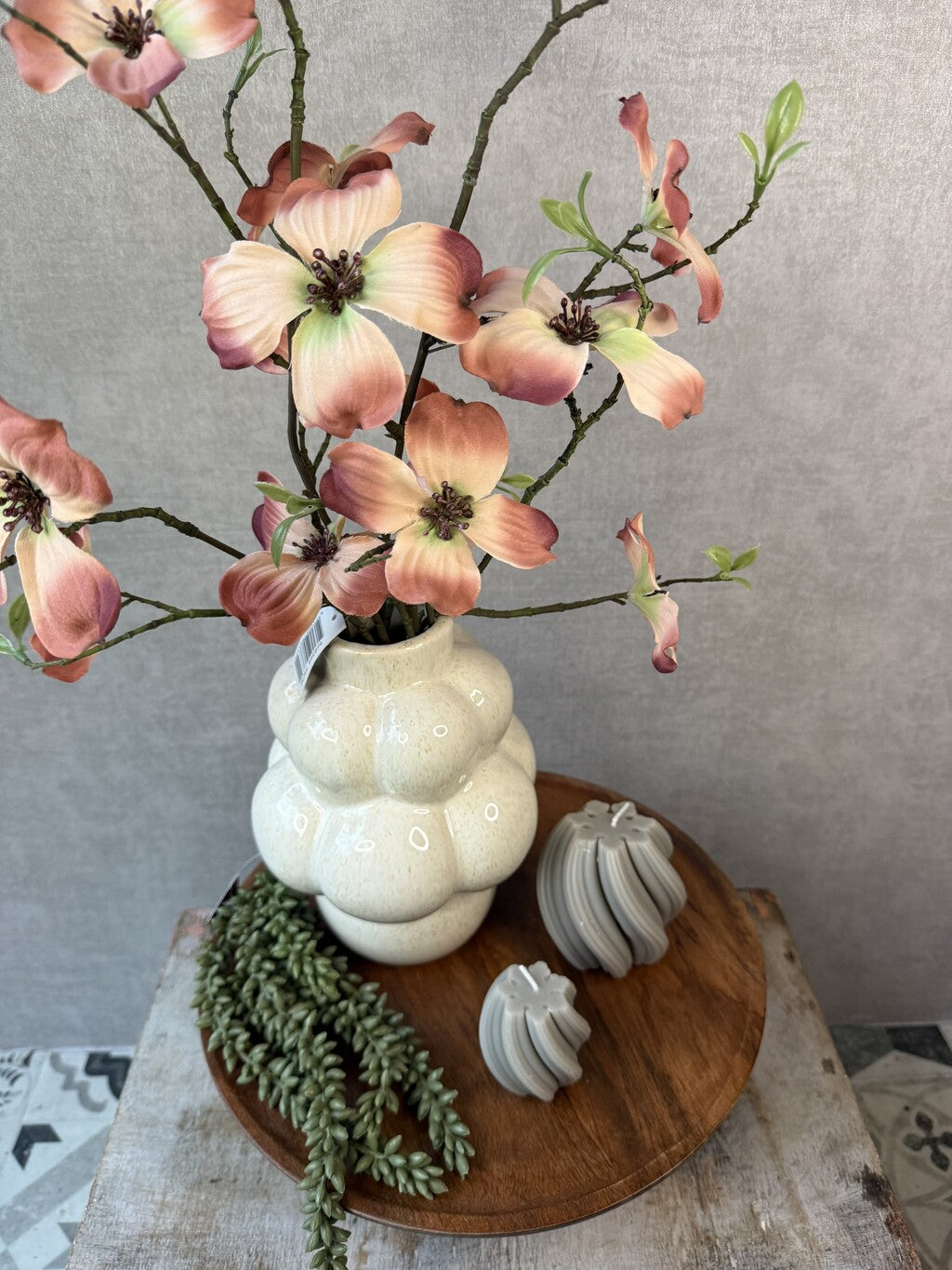 Tafel decoratie set Livara met houten dienblad, beige vaas, kleurrijke kunstbloemen, groene hangplant en decoratieve kaarsen.