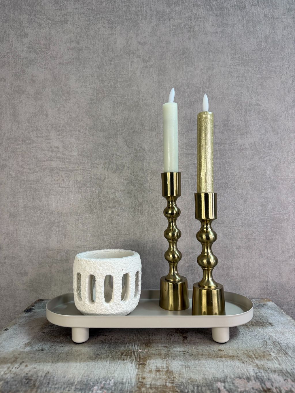 Beige metalen tray met een langwerpig ontwerp en lage rand met accessoires, geplaatst op een houten ondergrond tegen een neutrale achtergrond.