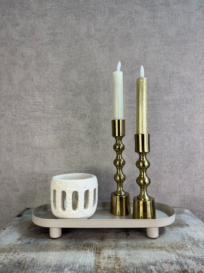 Beige metalen tray met een langwerpig ontwerp en lage rand met accessoires, geplaatst op een houten ondergrond tegen een neutrale achtergrond.