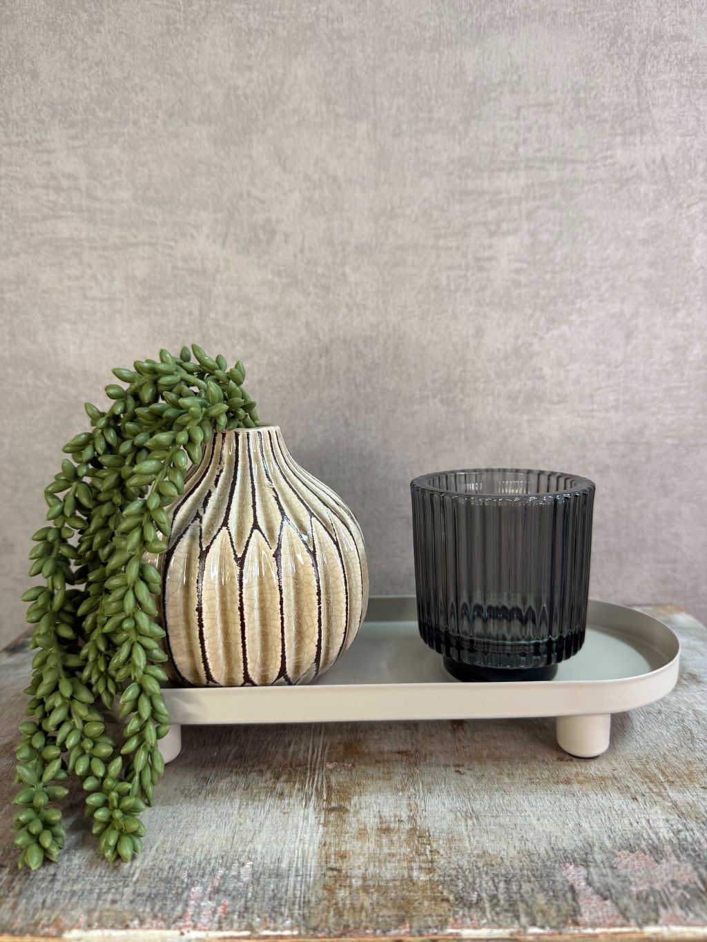 Beige metalen tray met een langwerpig ontwerp en lage rand met accessoires, geplaatst op een houten ondergrond tegen een neutrale achtergrond.