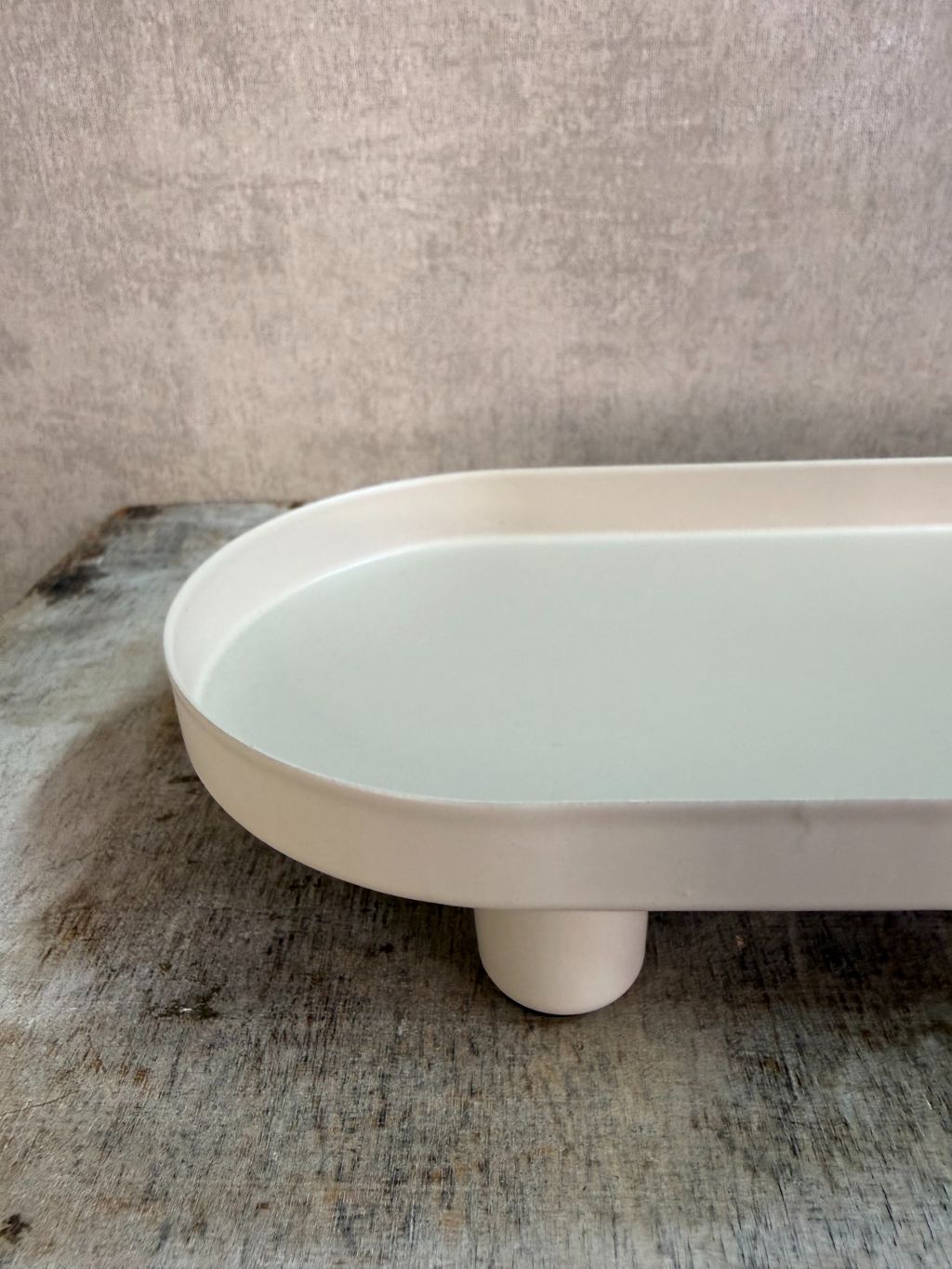 Beige metalen tray met een langwerpig ontwerp en lage rand, geplaatst op een houten ondergrond tegen een neutrale achtergrond.