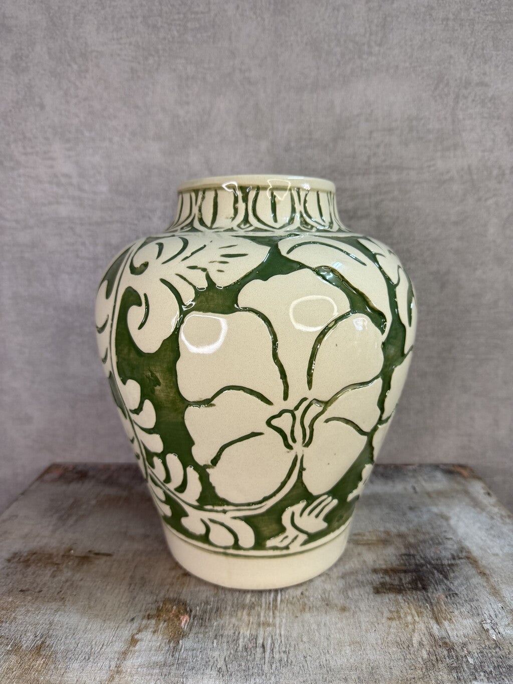 Beige keramieken vaas met groen bloemmotief van Mica op een houten ondergrond.