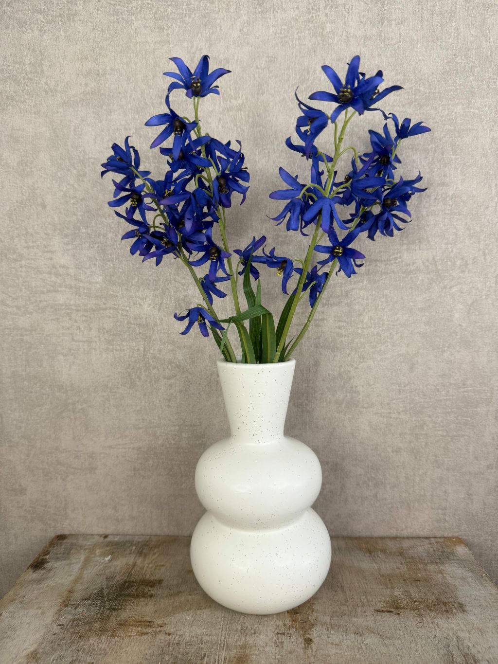 Witte keramieken vaas met zwarte spikkels en bolvormig design met blauwe kunstbloemen