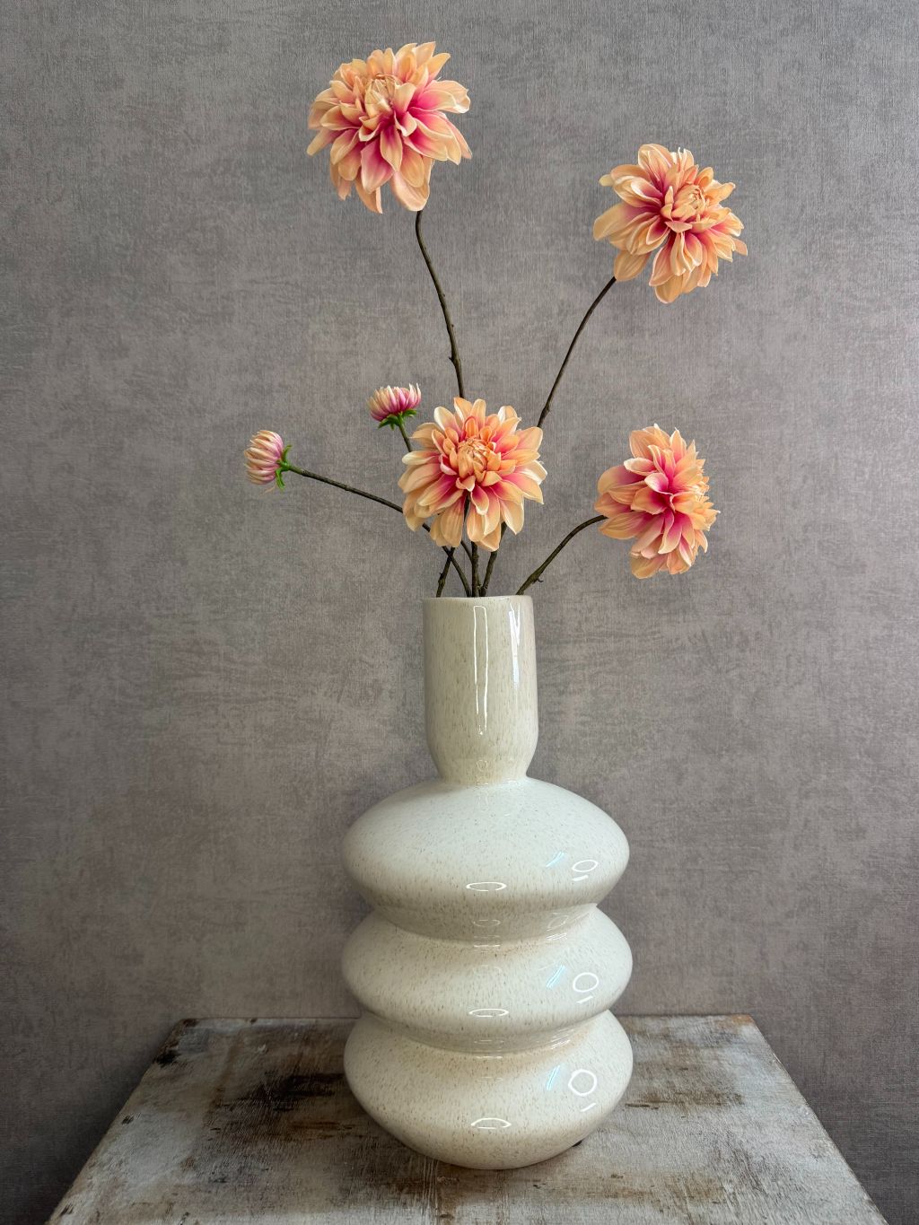 Vaas Disk – beige aardewerken vaas met golvende vorm, gestyled met oranje kunstbloemen.