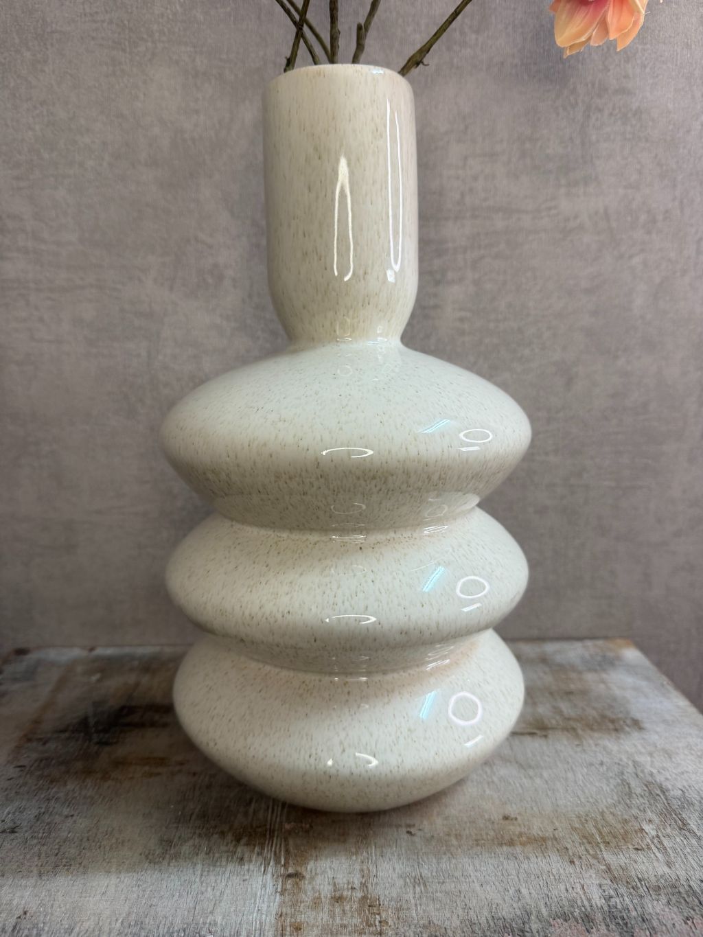 Vaas Disk – beige aardewerken vaas met golvende vorm, gestyled met oranje kunstbloemen.