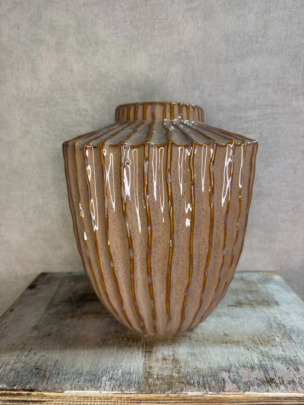 Keramieken vaas in oudroze en bruin met verticaal reliëf en glanzende afwerking, geplaatst op een houten ondergrond.