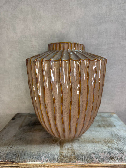 Keramieken vaas in oudroze en bruin met verticaal reliëf en glanzende afwerking, geplaatst op een houten ondergrond.