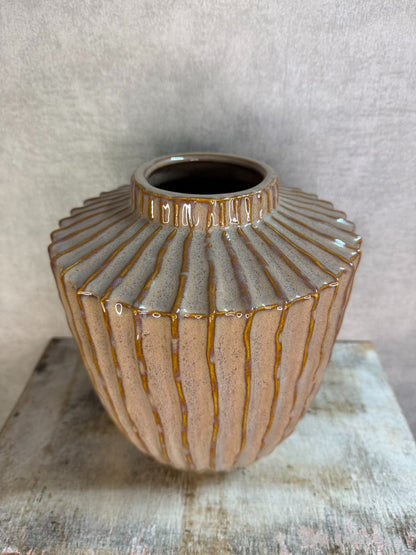 Keramieken vaas in oudroze en bruin met verticaal reliëf en glanzende afwerking, geplaatst op een houten ondergrond.