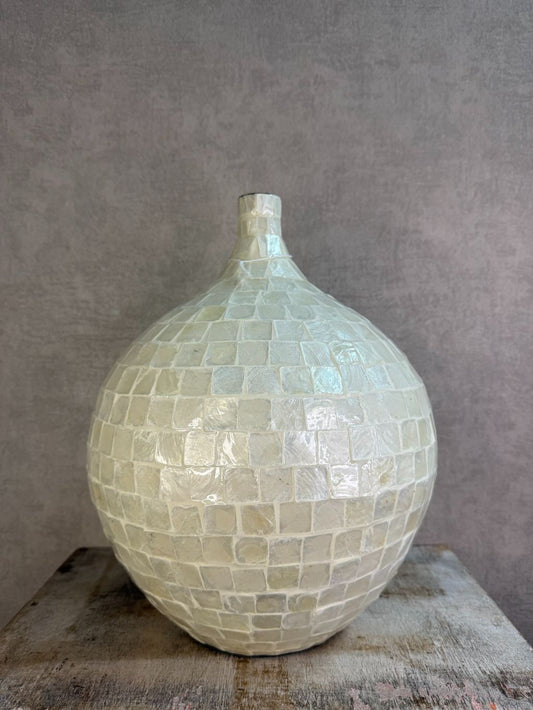 Ronde vaas met schelpmozaïek in crèmekleur, met smalle hals, geplaatst op een houten ondergrond tegen een neutrale achtergrond.