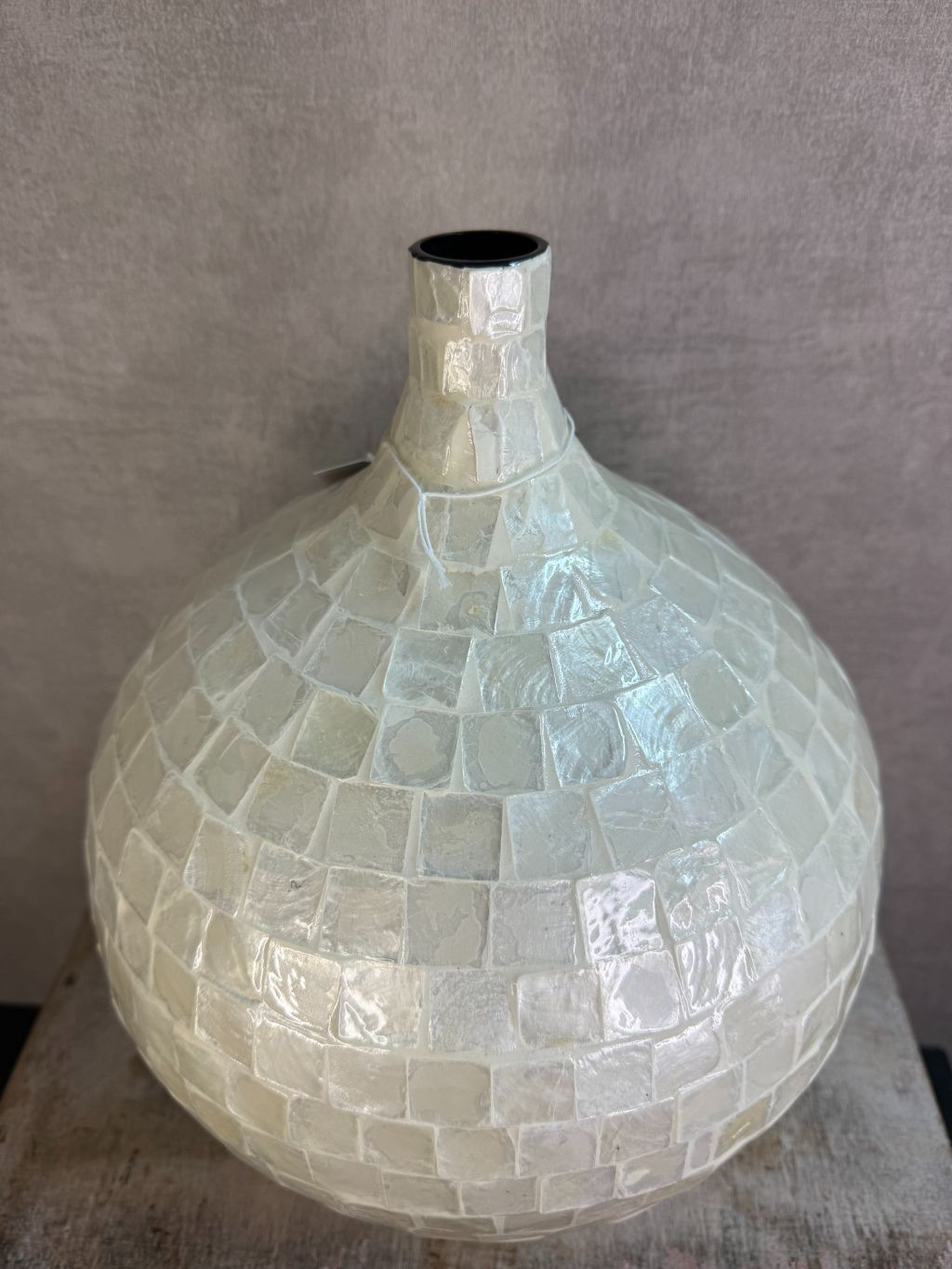 Ronde vaas met schelpmozaïek in crèmekleur, met smalle hals, geplaatst op een houten ondergrond tegen een neutrale achtergrond.