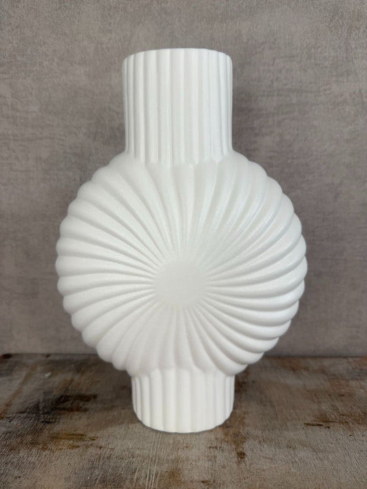 Witte keramieken vaas met ribbelpatroon en sculpturale vorm op houten ondergrond tegen een neutrale achtergrond.