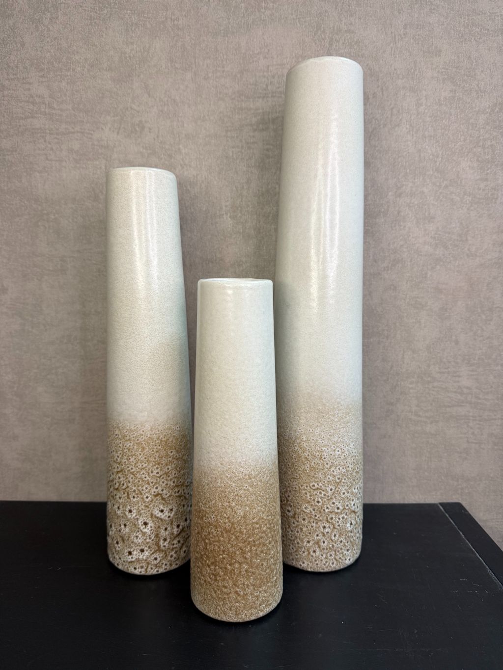 Keramieken vaas met crème-bruin kleurverloop en subtiel stippenreliëf, gepresenteerd in drie verschillende hoogtes.