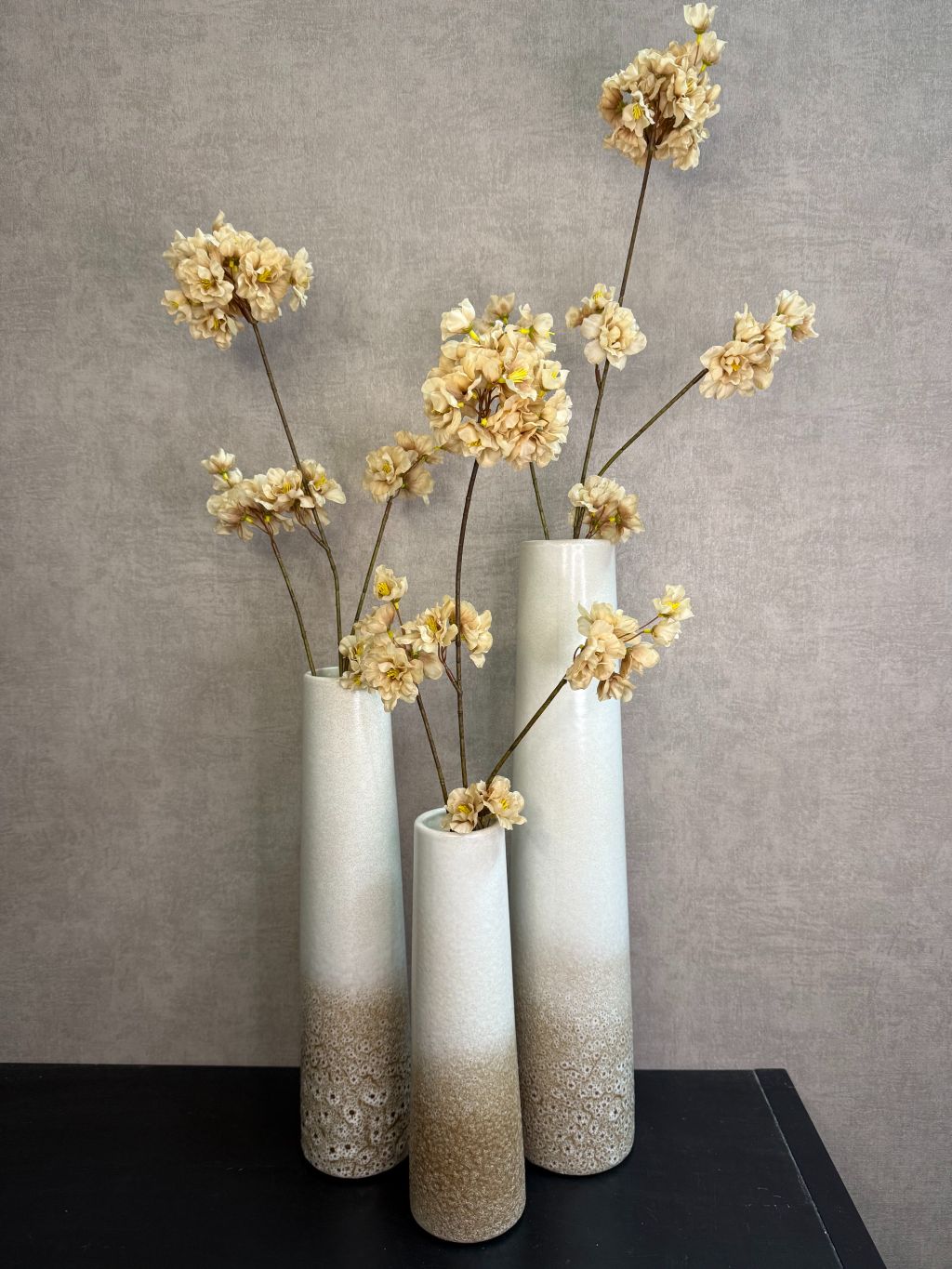 Keramieken vaas met crème-bruin kleurverloop en subtiel stippenreliëf, gepresenteerd in drie verschillende hoogtes met prachtige kunstbloemen