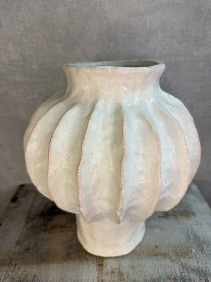 Beige keramieken vaas met organische ribstructuur op een houten ondergrond tegen een neutrale achtergrond.