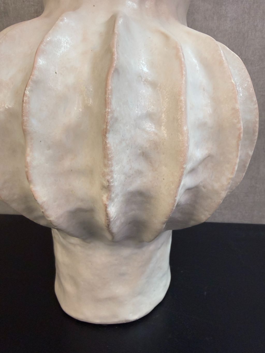 Beige keramieken vaas met organische ribstructuur op een houten ondergrond tegen een neutrale achtergrond.