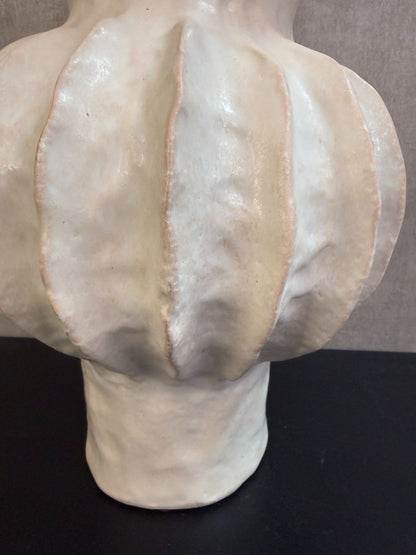 Beige keramieken vaas met organische ribstructuur op een houten ondergrond tegen een neutrale achtergrond.