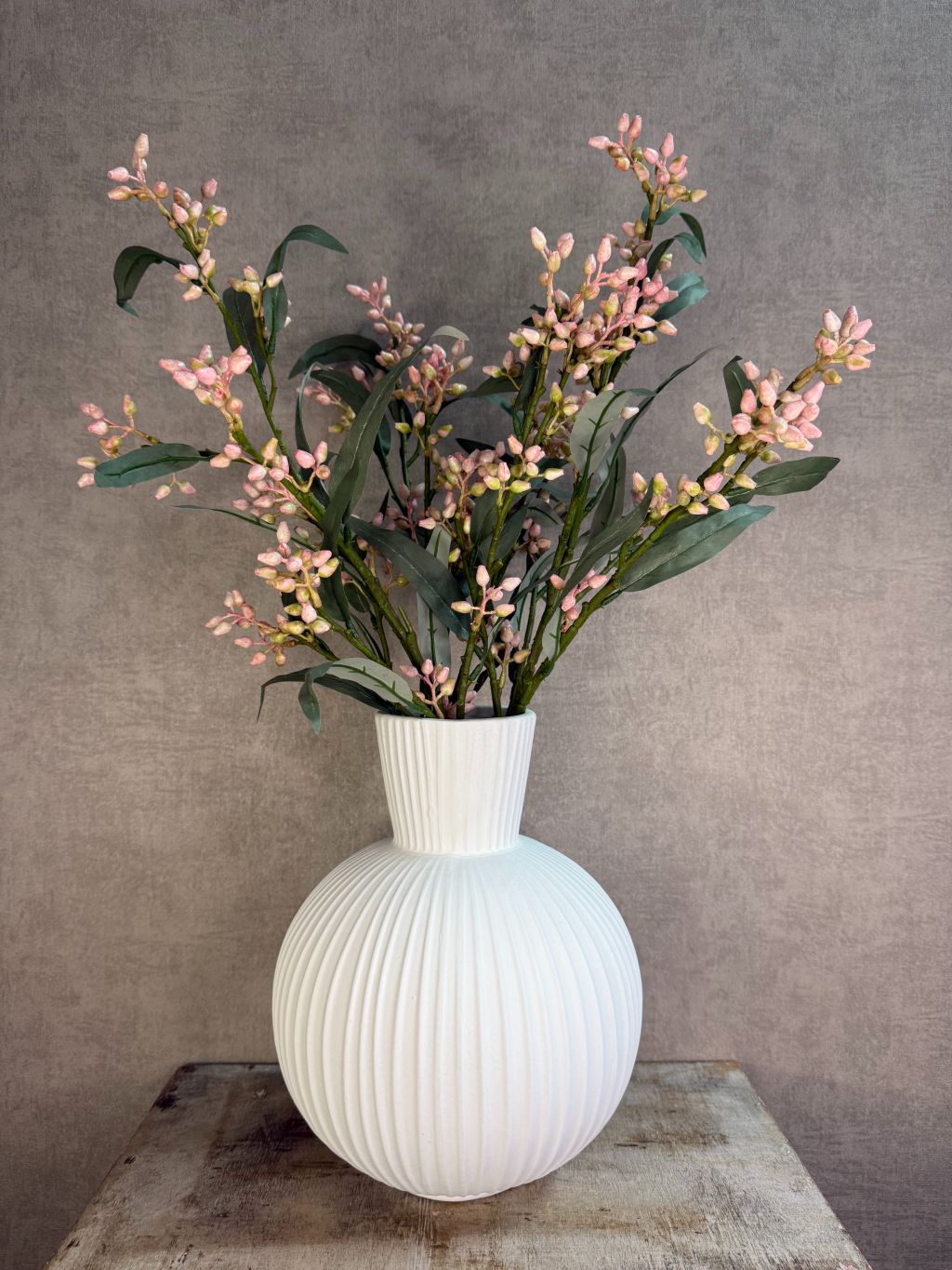 Witte keramieken vaas Jill met ronde vorm en verticaal ribbelpatroon op een houten ondergrond tegen een neutrale achtergrond met kunstbloemen