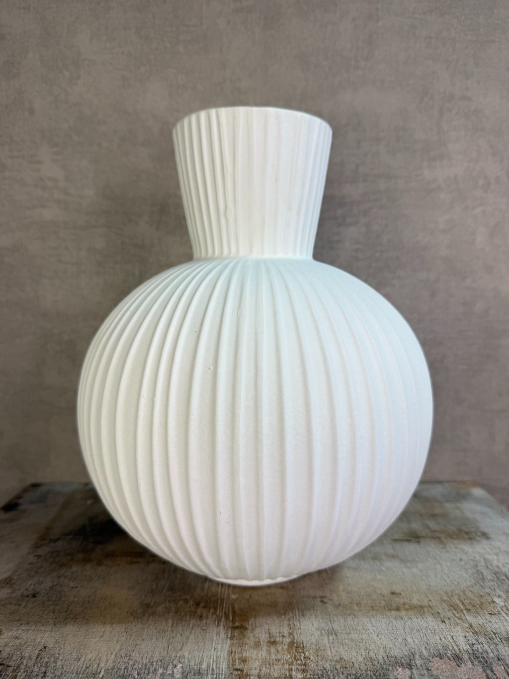 Witte keramieken vaas Jill met ronde vorm en verticaal ribbelpatroon op een houten ondergrond tegen een neutrale achtergrond.