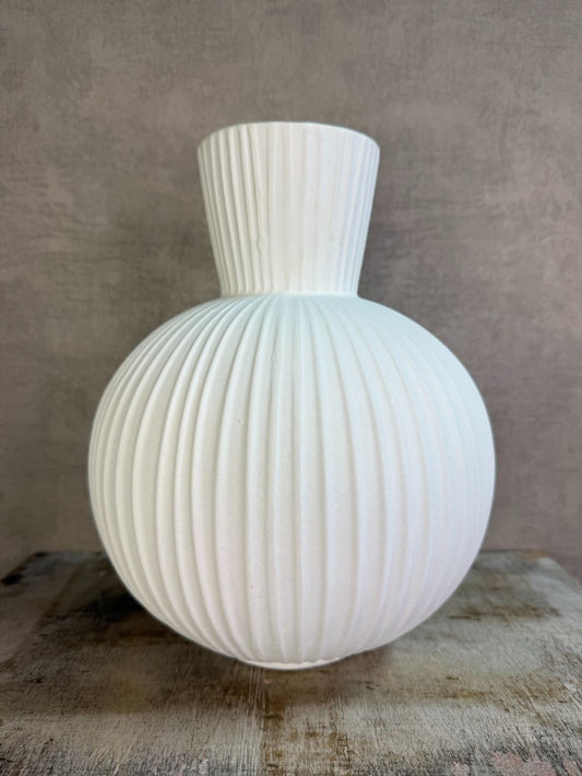 Witte keramieken vaas Jill met ronde vorm en verticaal ribbelpatroon op een houten ondergrond tegen een neutrale achtergrond.