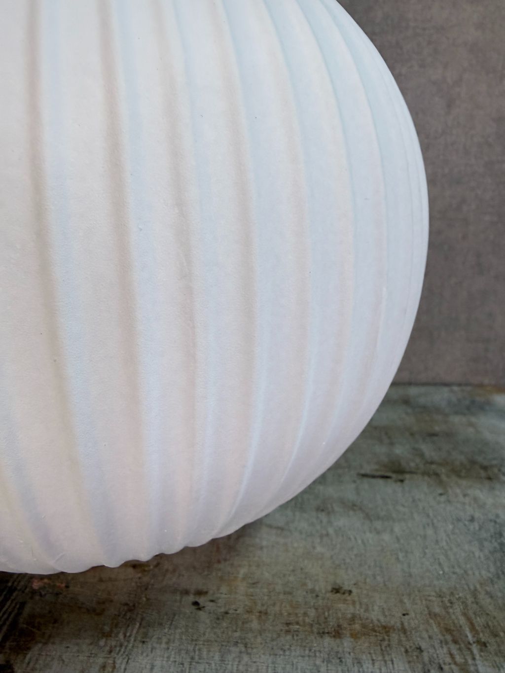 Witte keramieken vaas Jill met ronde vorm en verticaal ribbelpatroon op een houten ondergrond tegen een neutrale achtergrond.