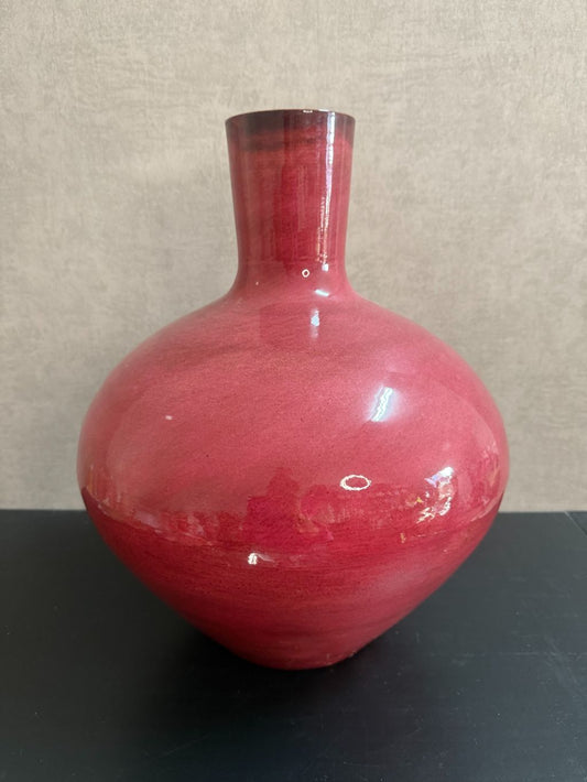 Roze glanzende metalen vaas met bolle vorm en smalle hals, staand op een zwart oppervlak.