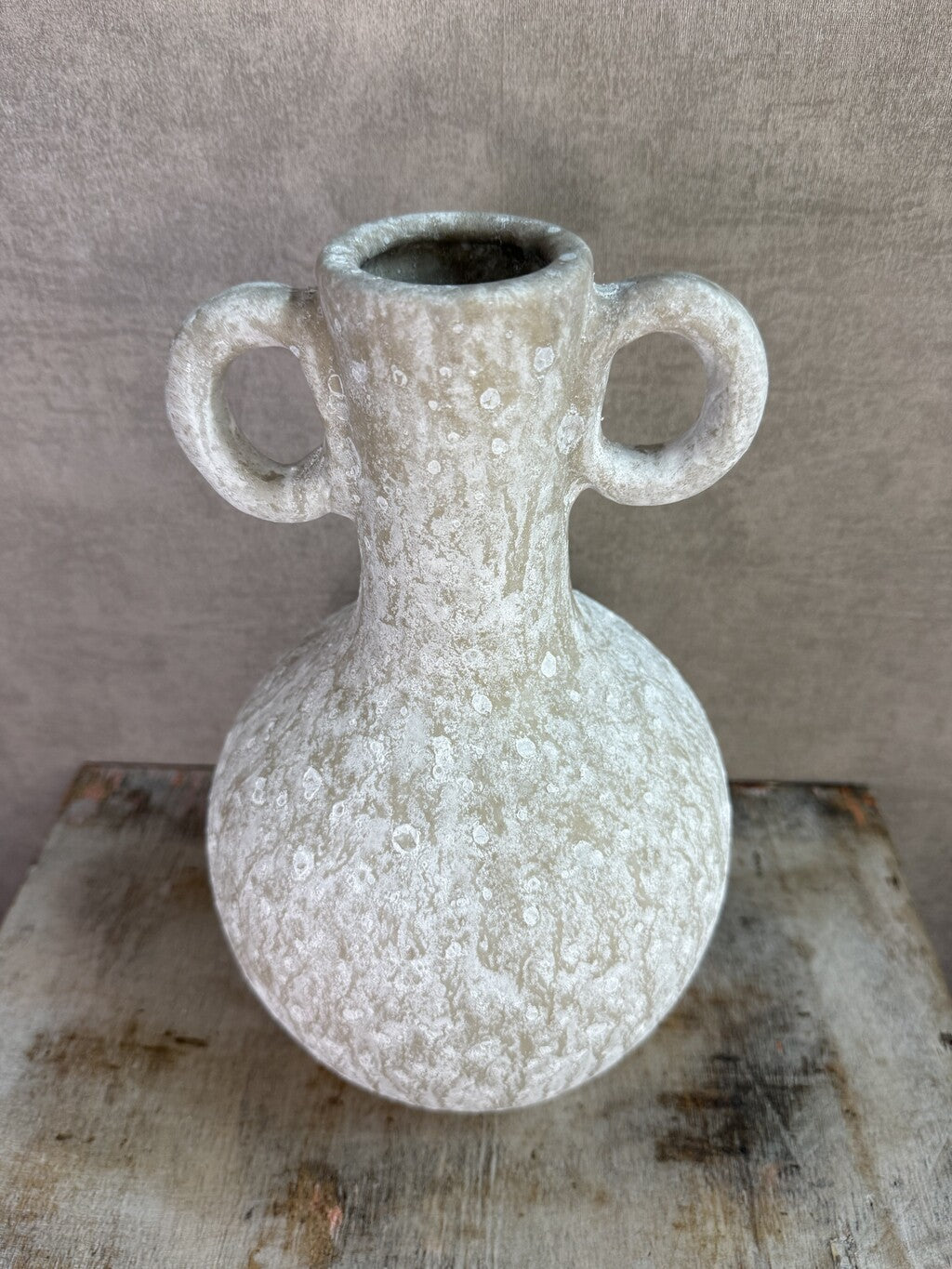 Beige keramieken kruikvaas met ronde vorm en twee decoratieve oren op een houten ondergrond.