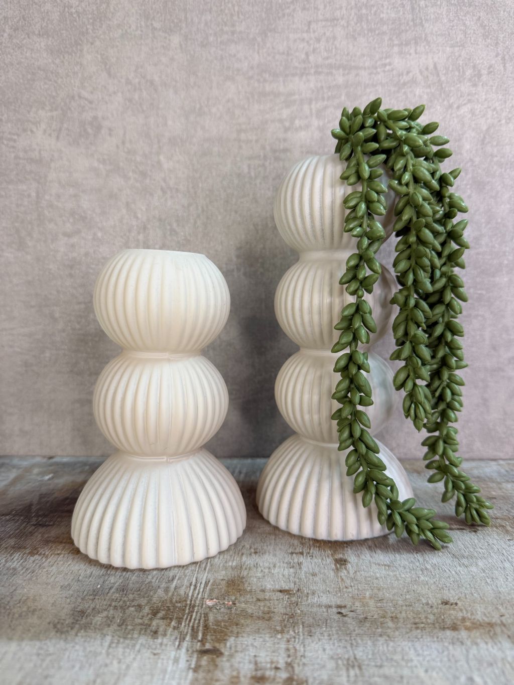 Crèmekleurige glazen vaas met ribbelstructuur en gestapelde vorm, geschikt voor bloemen, gefotografeerd op een houten ondergrond. met een kunst erwtenplantje.