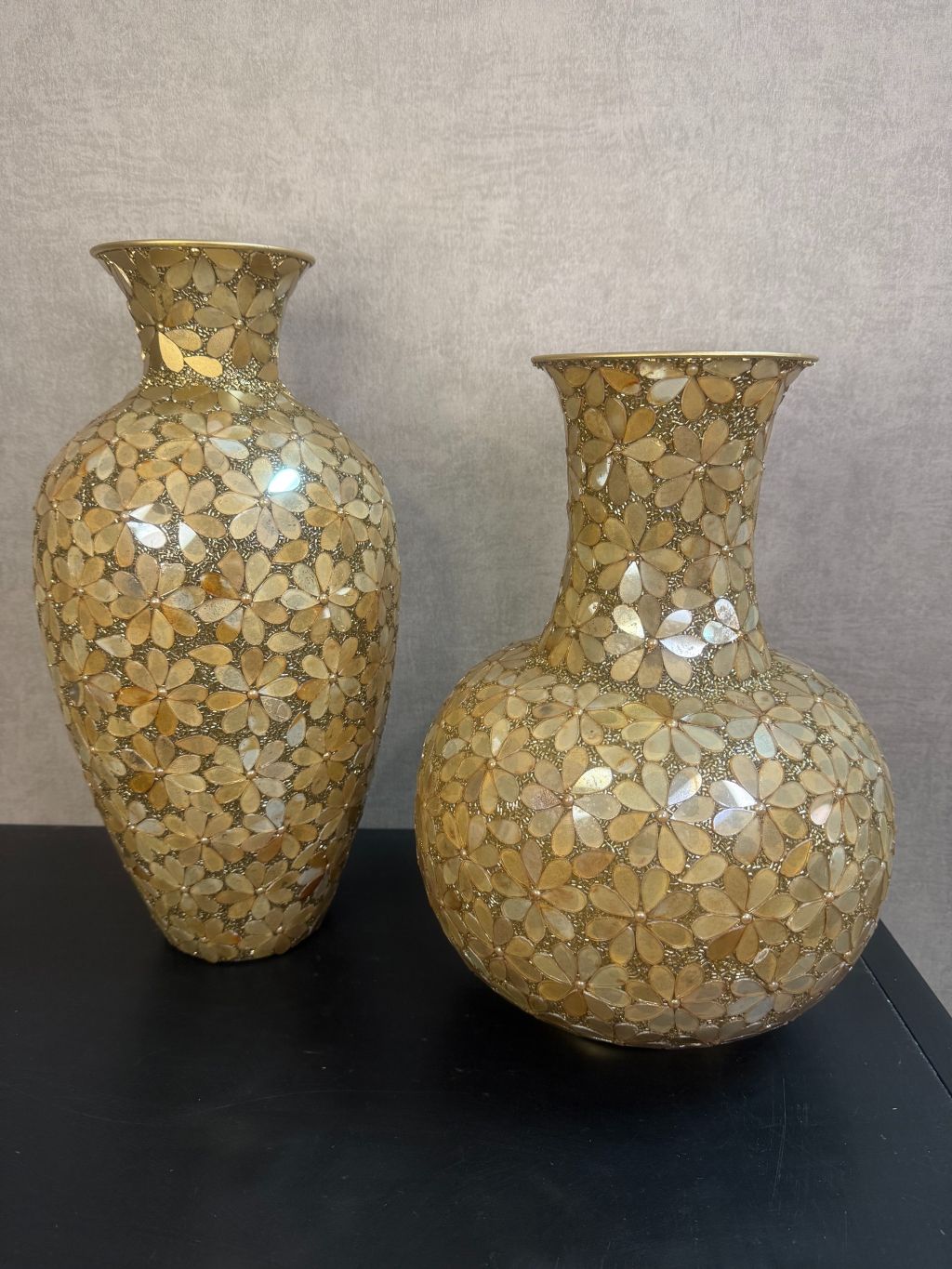 Gouden smalle vaas en bolvormige vaas met bloemmotief van metaal en glas op een houten ondergrond.