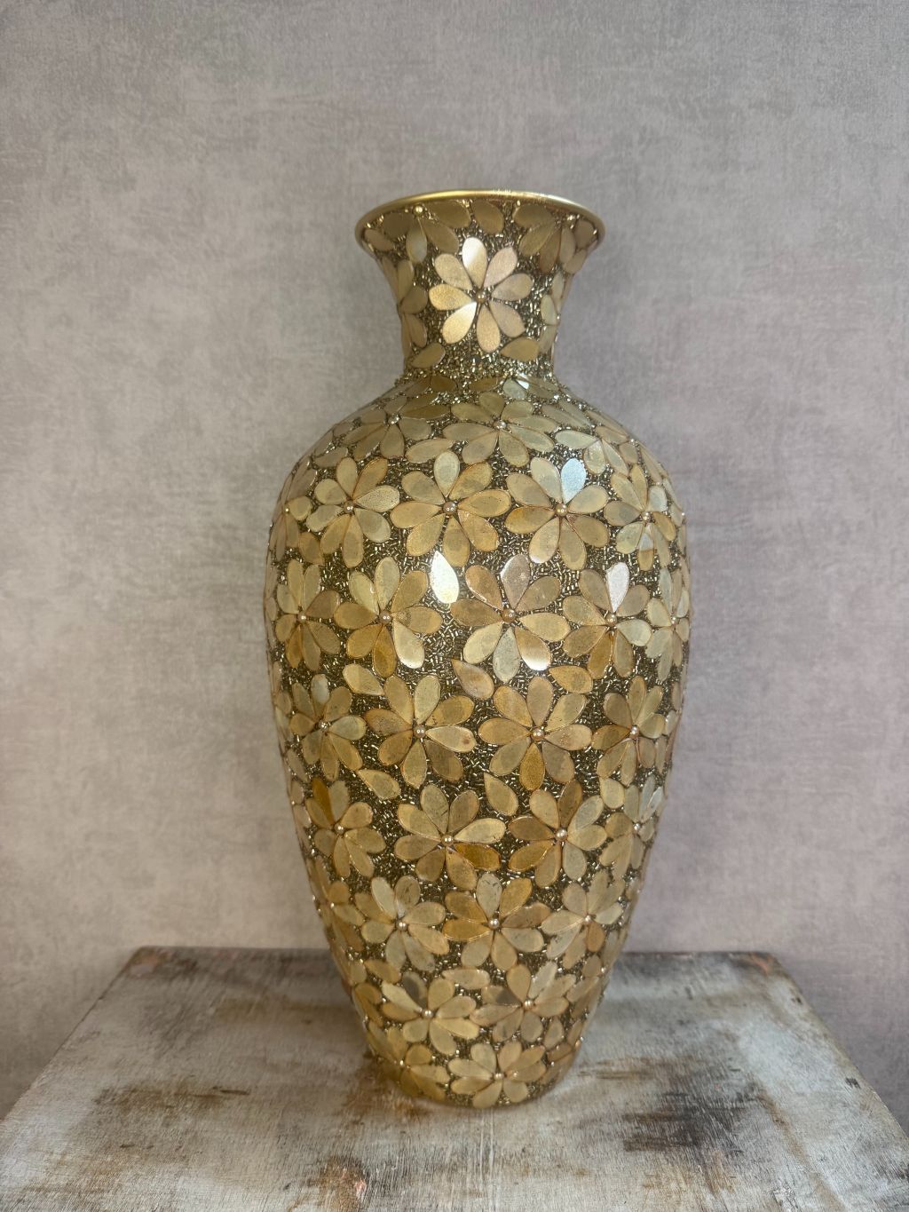 Gouden smalle vaas met bloemmotief van metaal en glas op een houten ondergrond.