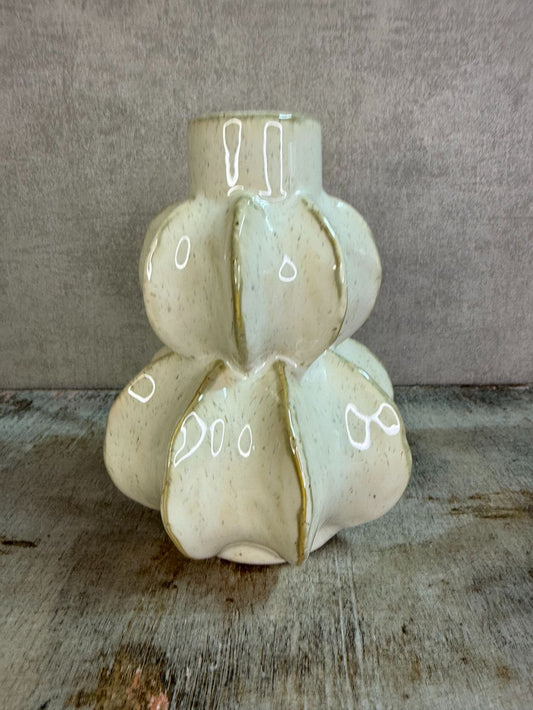 Beige keramieken vaas met organische vormen op een houten ondergrond.