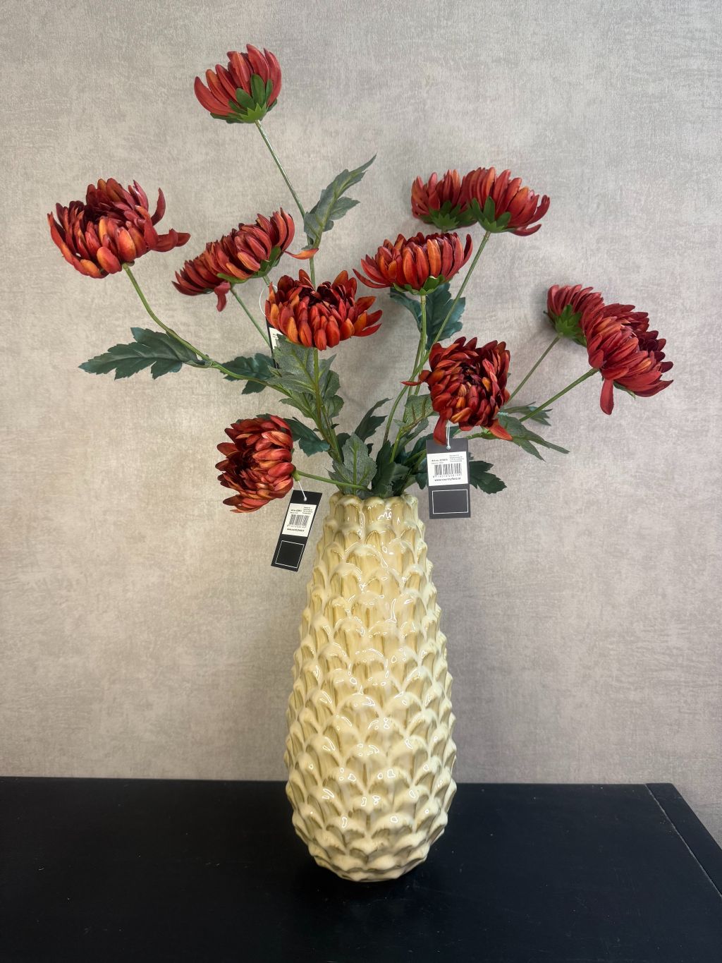 Vaas Pinecone beige – keramieken vaas met glanzende dennenappelstructuur op een houten ondergrond tegen een grijze muur. met prachtige kunstbloemen.