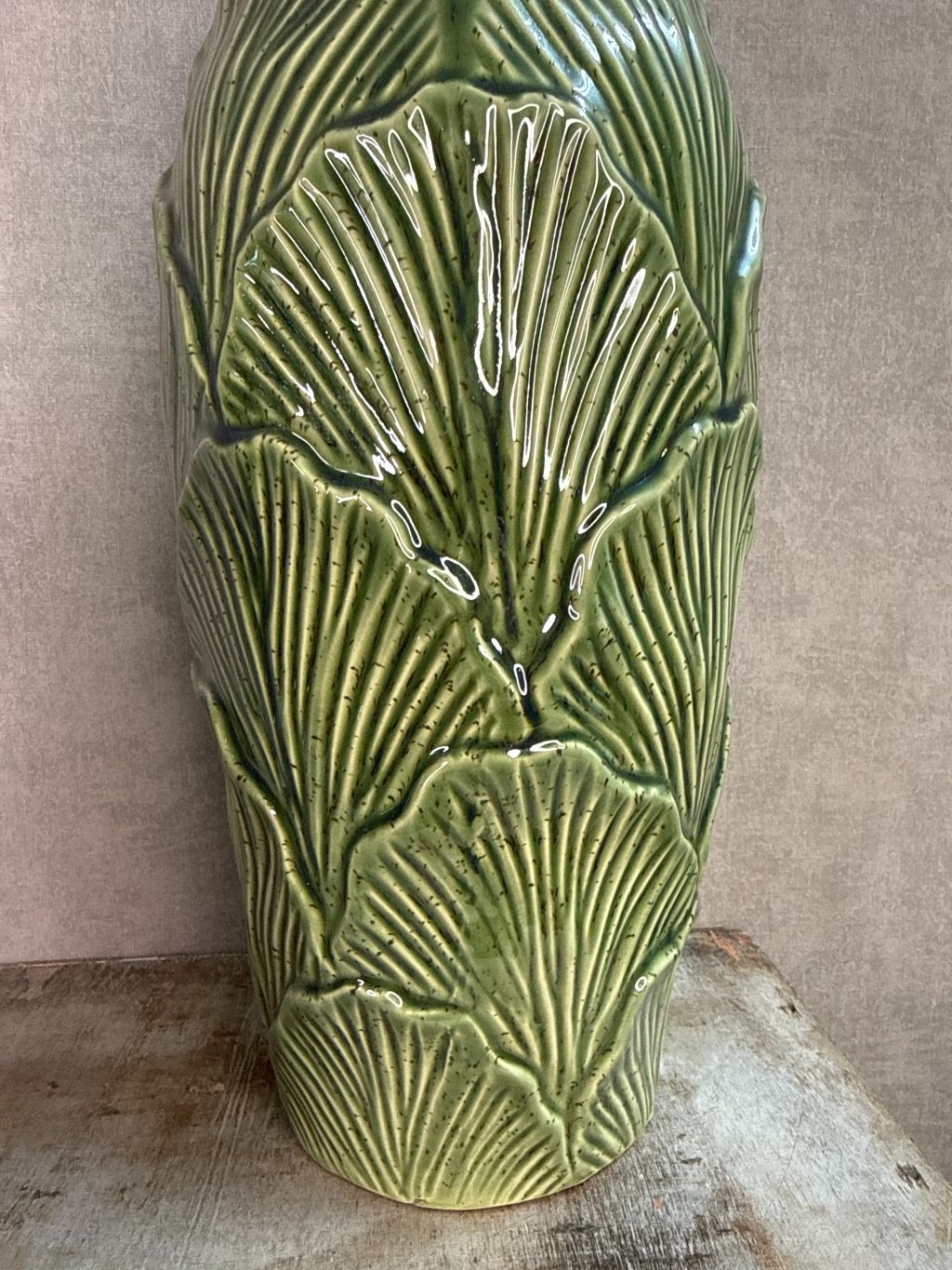 Groene keramieken vazen met bladstructuur in twee formaten op een houten ondergrond tegen een neutrale achtergrond.