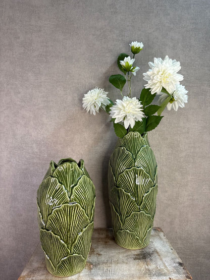 Groene keramieken vazen met bladstructuur in twee formaten op een houten ondergrond tegen een neutrale achtergrond.