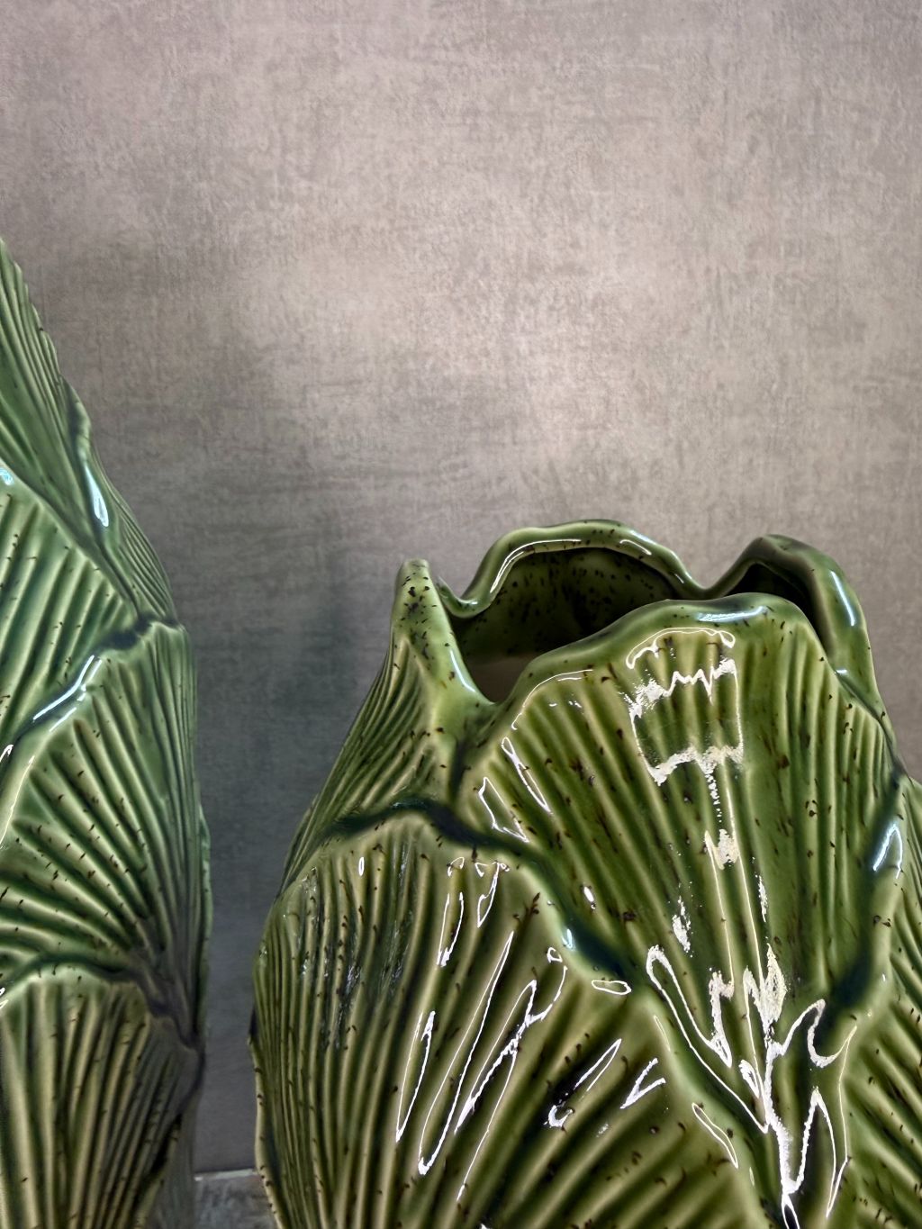 Groene keramieken vazen met bladstructuur in twee formaten op een houten ondergrond tegen een neutrale achtergrond.