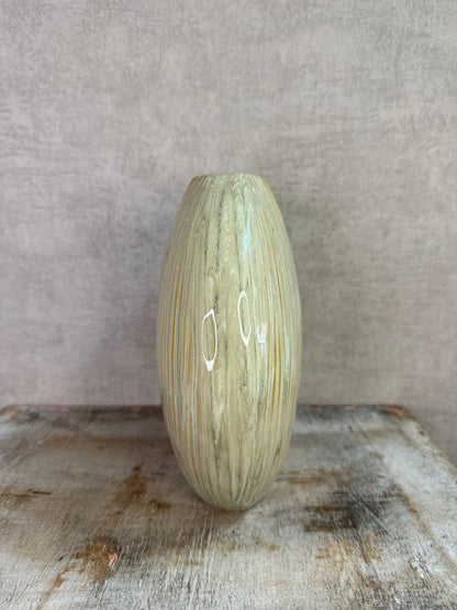 Groene keramieken vaas met subtiele verticale structuur op een houten ondergrond tegen een neutrale achtergrond.