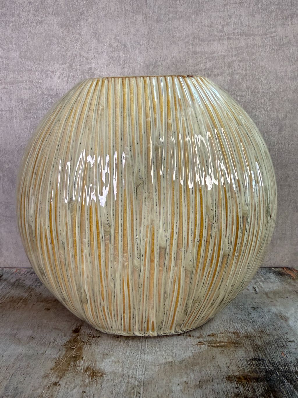 Groene keramieken vaas met subtiele verticale structuur op een houten ondergrond tegen een neutrale achtergrond.