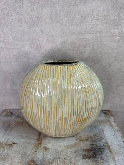 Groene keramieken vaas met subtiele verticale structuur op een houten ondergrond tegen een neutrale achtergrond.