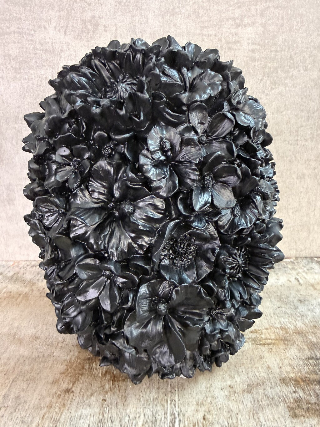 Zwarte polyresin vaas met bloemreliëf op een houten ondergrond.