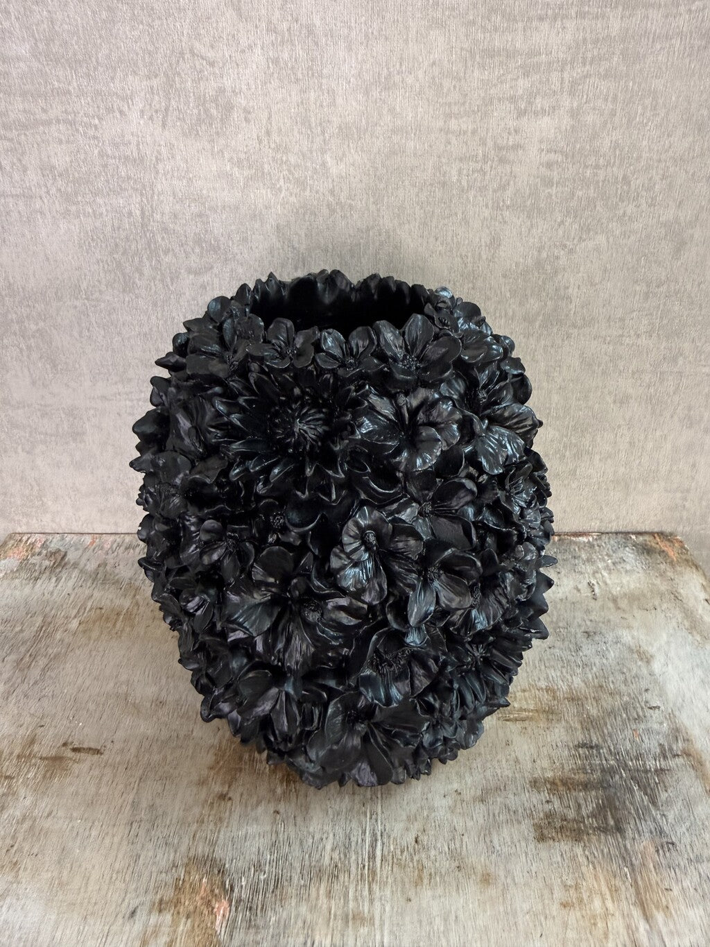 Zwarte polyresin vaas met bloemreliëf op een houten ondergrond.