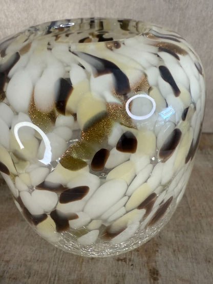 Glazen vaas met gevlekt patroon in beige, wit, bruin en goud, staand op houten oppervlak tegen een neutrale achtergrond.