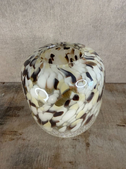 Glazen vaas met gevlekt patroon in beige, wit, bruin en goud, staand op houten oppervlak tegen een neutrale achtergrond.