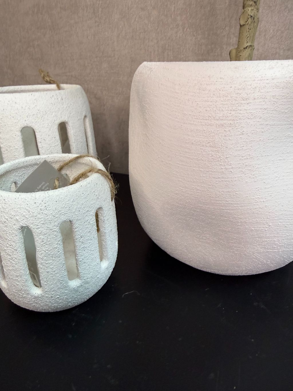 Kunst olijfboom in witte keramieken pot met twee witte waxinelichthouders op een zwarte tafel