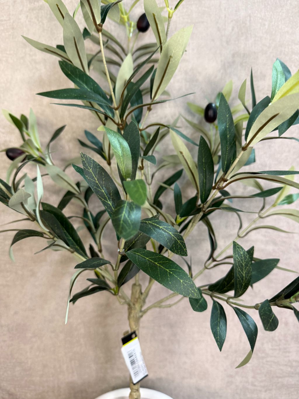 Kunst olijfboom in witte keramieken pot met twee witte waxinelichthouders op een zwarte tafel