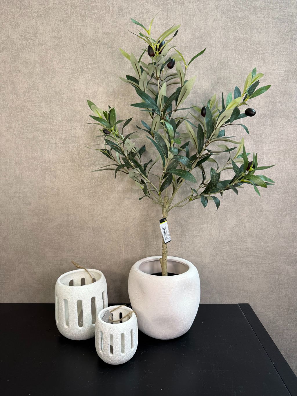Kunst olijfboom in witte keramieken pot met twee witte waxinelichthouders op een zwarte tafel