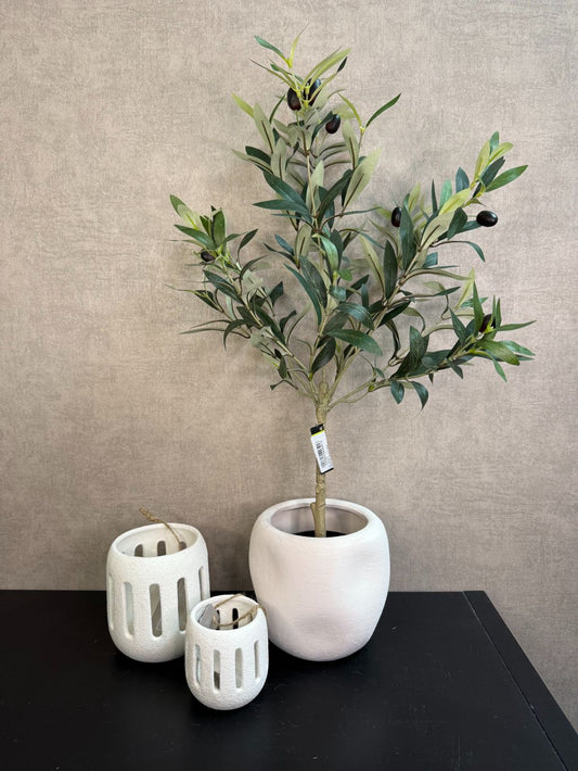 Kunst olijfboom in witte keramieken pot met twee witte waxinelichthouders op een zwarte tafel