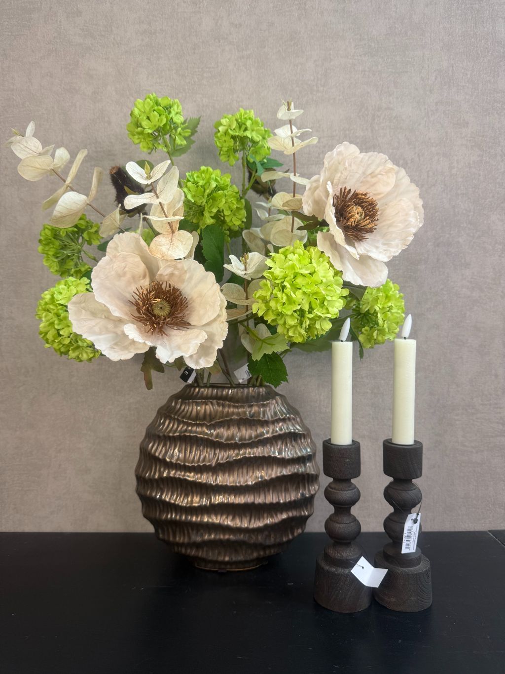 Vensterbank decoratie set Meave – bronzen vaas met groene en crème bloemen, houten kandelaars met LED-kaarsen op zwarte ondergrond.