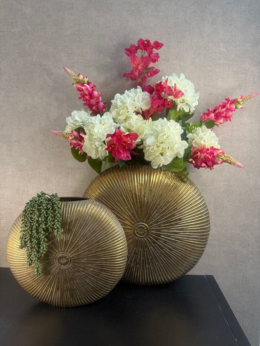 Decoratieset met twee ronde gouden vazen, wit-roze kunstbloemen en een hangend kunstplantje, gestyled als blikvanger op een zwarte ondergrond.