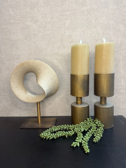 Vensterbankdecoratie met sculpturaal ornament, LED-kaarsen op metalen houders en een groene kunst erwtenplant op een zwarte ondergrond.