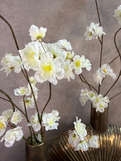 Twee goudkleurige decoratieve vazen met witte bloesemtakken op een zwarte ondergrond tegen een neutrale achtergrond.