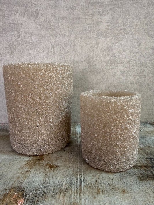 Set van twee zandkleurige waxinelichthouders met steentjesstructuur in verschillende formaten op een houten ondergrond.